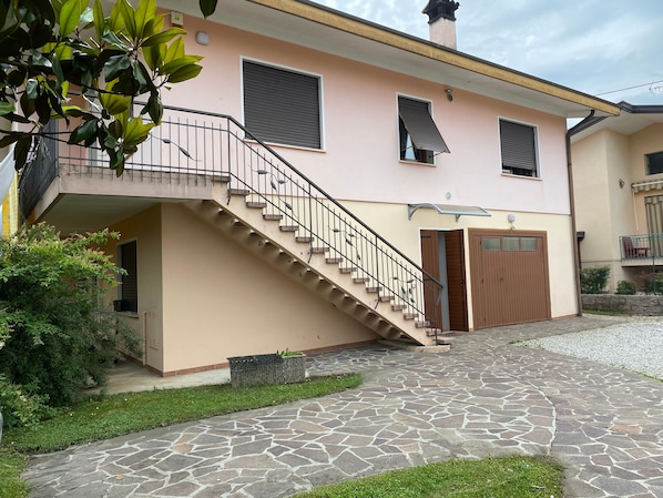 Una casa de dos pisos con un camino de entrada empedrado de piedra, una puerta de madera y una escalera con barandilla metálica.