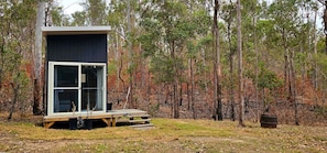 A modern cabin with a large glass window, surrounded by a forest.