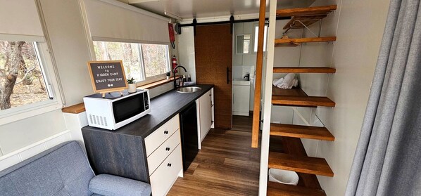 A compact kitchen with a microwave, sink, and wooden shelves.