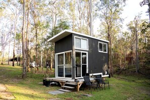 A modern cabin with a flat roof, large windows, and a deck with outdoor seating.