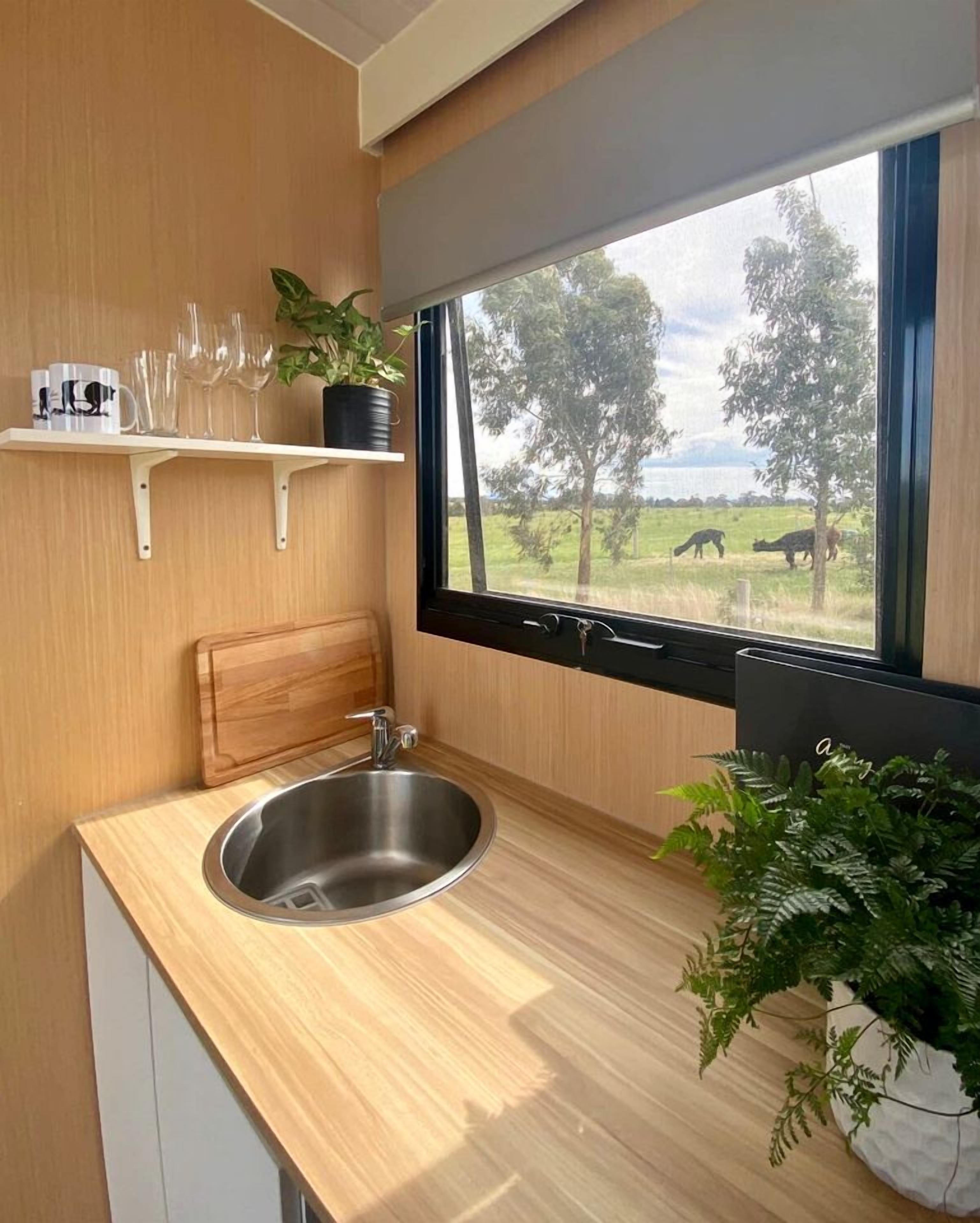 A compact kitchen with a stainless steel sink, wooden countertop, and a window overlooking a grassy area with trees.