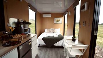 A compact room with a bed, bedside table, and a small kitchenette.