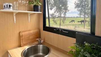 A compact kitchen with a stainless steel sink, wooden countertop, and a window overlooking a grassy area with trees.
