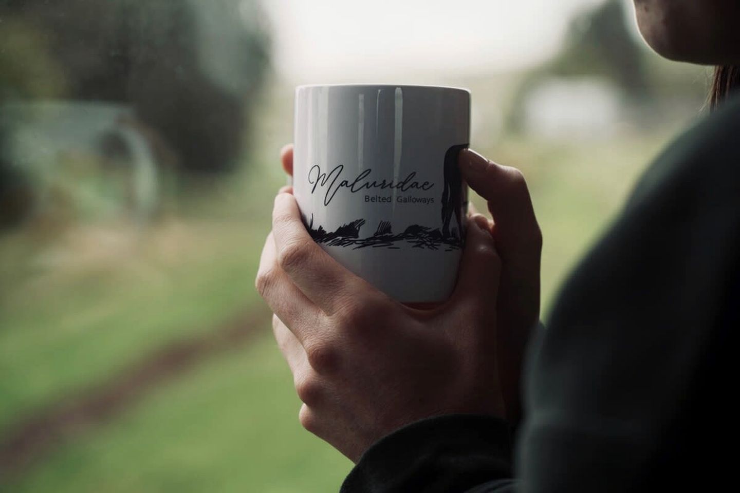Una persona sosteniendo una taza con un diseño de paisaje.