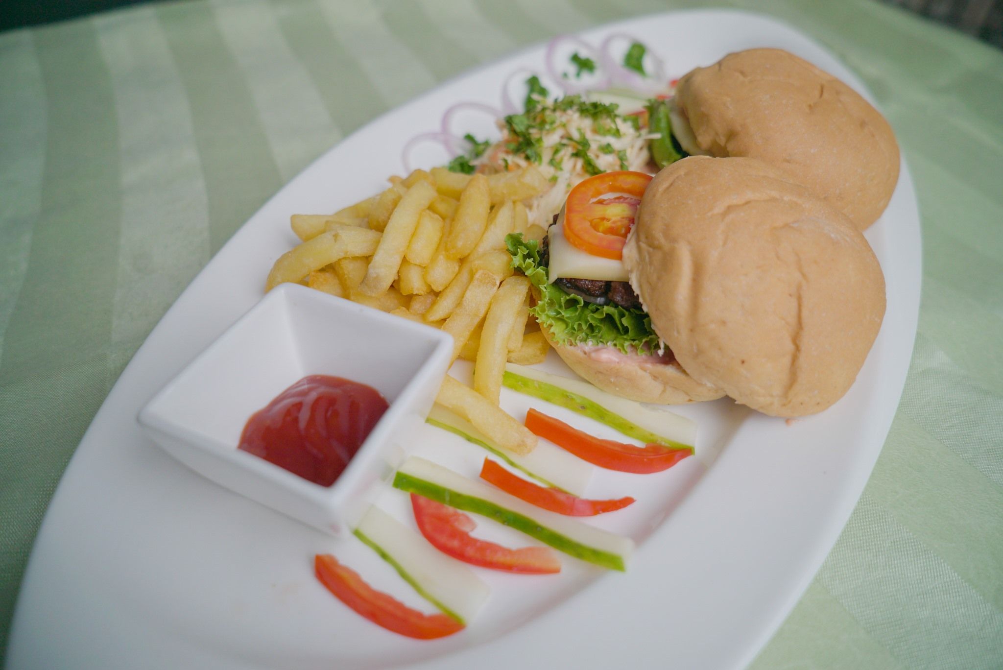 Un plato con una hamburguesa, papas fritas y un recipiente pequeño de kétchup.