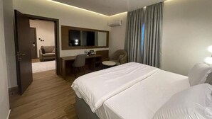 A hotel room with a large bed, a desk, a chair, a small table, and a mirror. - Paris Arena Holiday Inn (Abuja)