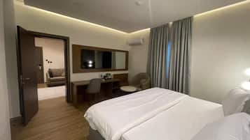 A hotel room with a large bed, a desk, a chair, a small table, and a mirror.