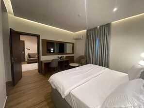 Habitación de hotel con una cama grande, un escritorio, una silla, una mesita y un espejo.