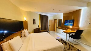 A hotel room with a large bed, a desk with a chair, a television, and a door leading to another room. - Paris Arena Holiday Inn (Abuja)