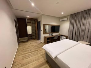 A hotel room with a bed, desk, chair, and a wardrobe. - Paris Arena Holiday Inn (Abuja)
