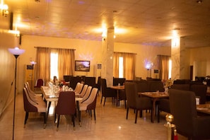 A restaurant with a long table set for dining, multiple chairs, and a television on the wall. - Paris Arena Holiday Inn (Abuja)