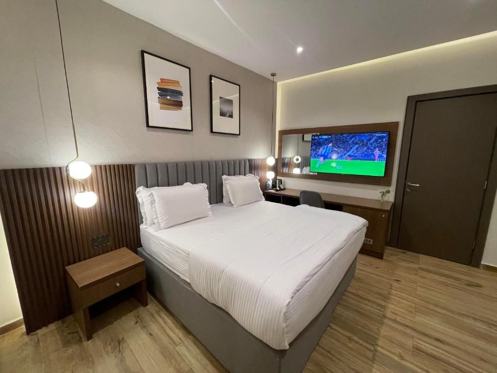 Habitación de hotel moderna con una cama grande, mesita de noche y televisor montado en la pared.
