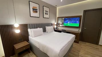 Habitación de hotel moderna con una cama grande, mesita de noche y televisor montado en la pared.