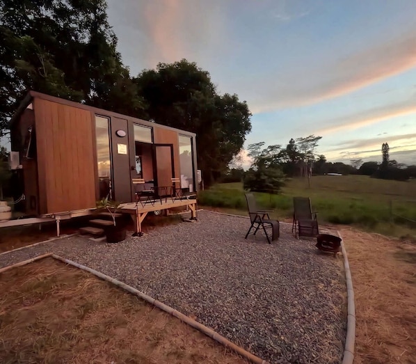 A modern wooden cabin with a deck, outdoor seating, and a gravel patio.
