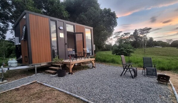 A modern cabin with a deck, outdoor seating, and a gravel ground.