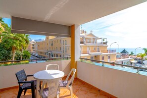 Ein Balkon mit Tisch und Stühlen mit Blick auf eine Straße mit Gebäuden und parkenden Autos.