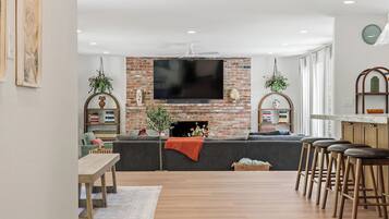 Een moderne woonkamer met een bakstenen open haard, een flatscreen televisie, een eethoek met een houten tafel en een bar met krukken.