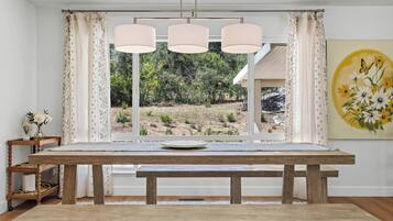 A dining area with a wooden table, three pendant lights, and a view of a garden through a window.