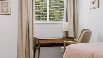 Ein Schlafzimmer mit einem Bett, einem Schreibtisch, einem Stuhl, einem Fenster mit Jalousien und einer Lampe.