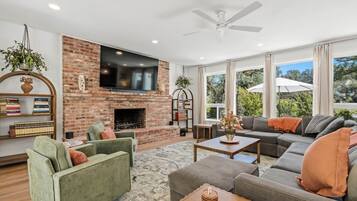 A modern living room with a brick fireplace, a flat-screen TV, and a large window offering a view of the outdoors.