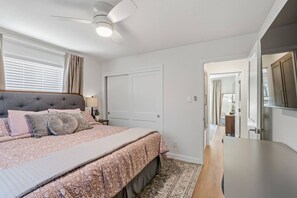 Une chambre à coucher avec un lit, un ventilateur de plafond, une porte et une vue sur une autre pièce.