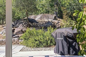 Un espace patio doté d’un barbecue recouvert d’une housse de protection à l’effigie de la marque, entouré de rochers et de verdure.