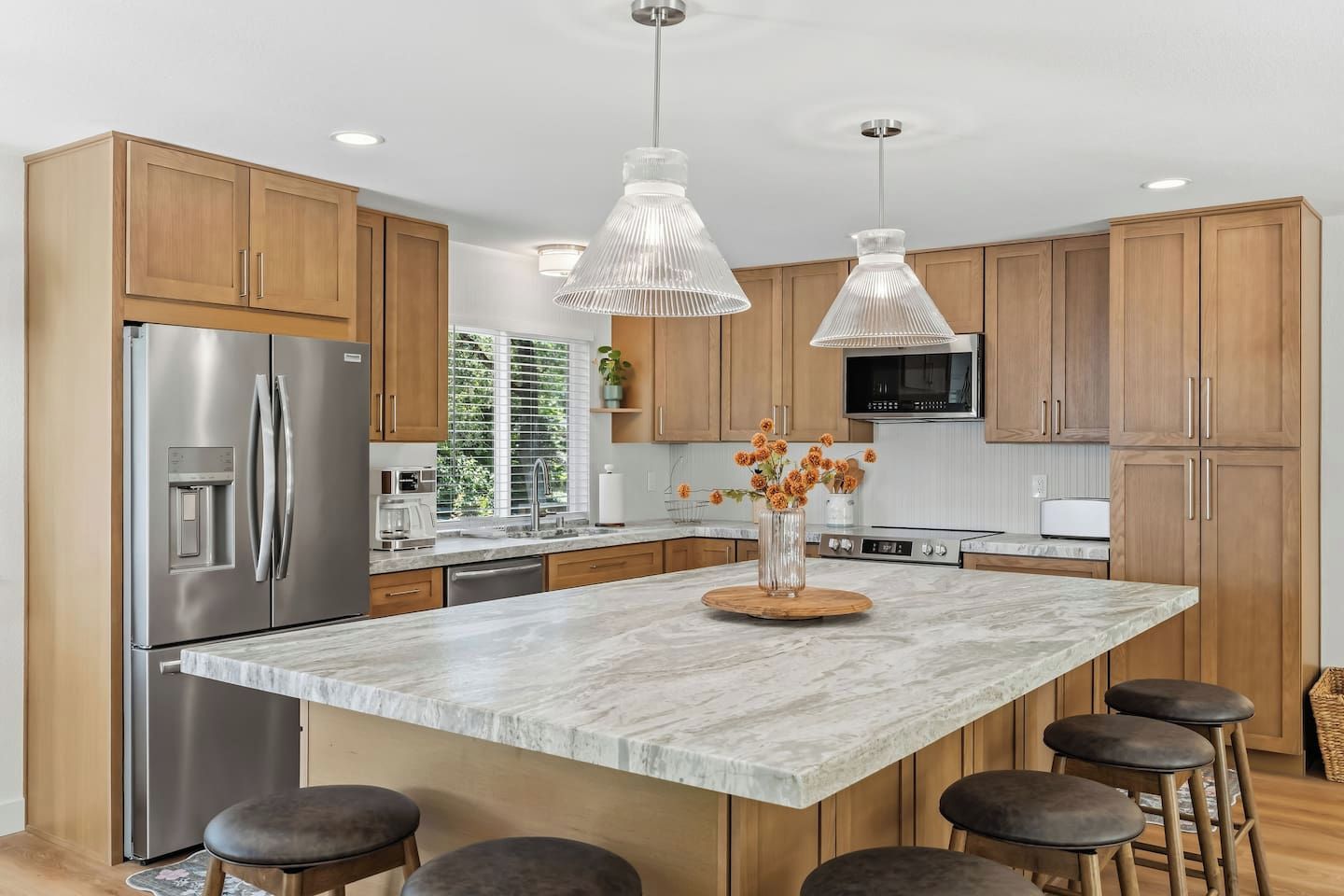 A modern kitchen with a large island, stainless steel appliances, wooden cabinets, and pendant lighting.