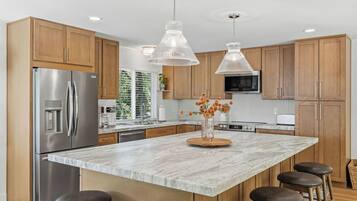 A modern kitchen with a large island, stainless steel appliances, wooden cabinets, and pendant lighting.