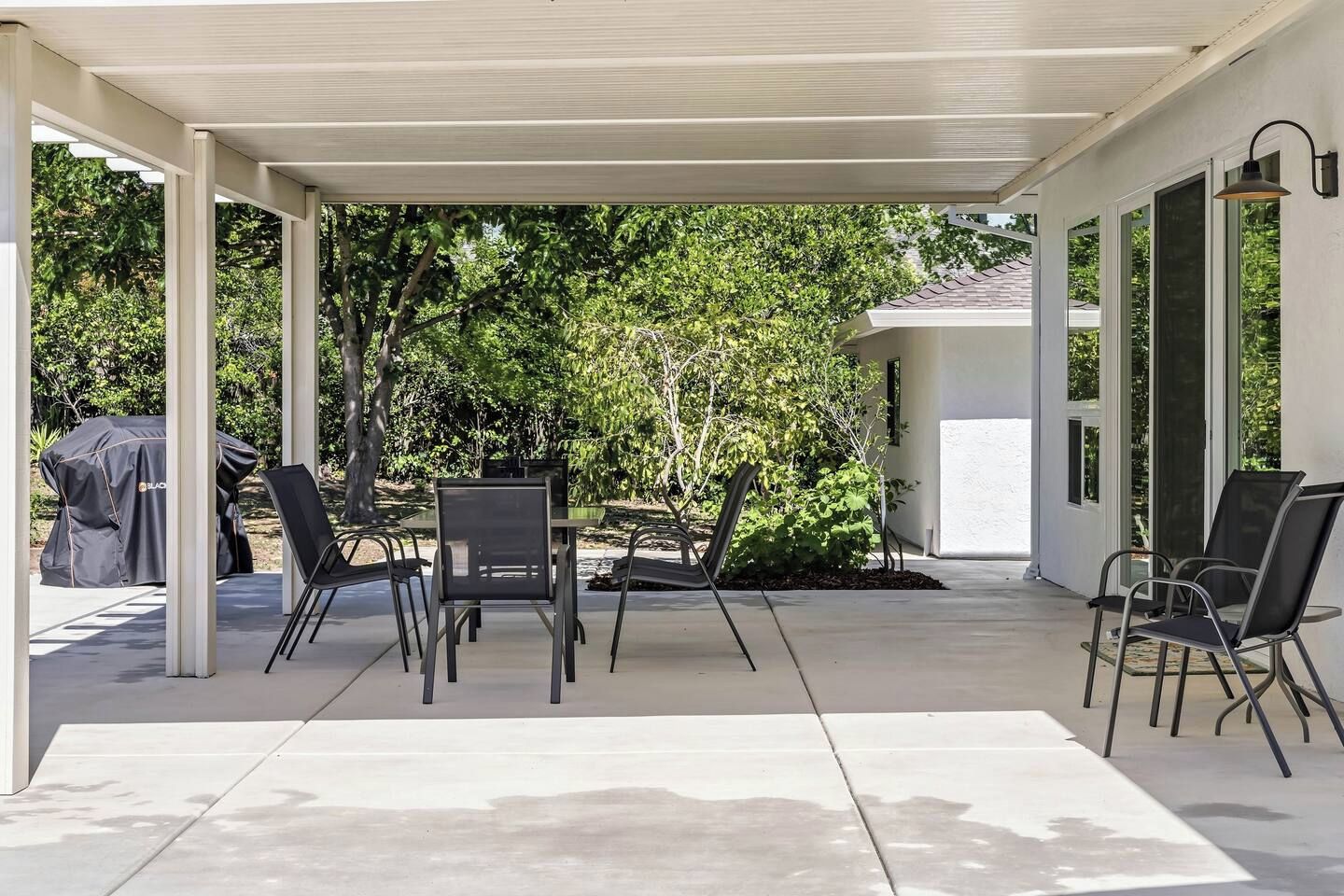 An outdoor patio with a covered seating area, a grill, and a view of the surrounding greenery.