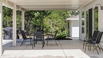 An outdoor patio with a covered seating area, a grill, and a view of the surrounding greenery.