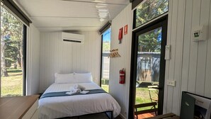 A bedroom with a bed, a small table, a fire extinguisher, and a view of the outdoors. - Fantastic Tiny House Perfect for Families with Swimming Pool, Game Room and Tennis Court in Victoria, Australia (Dadswells Bridge)