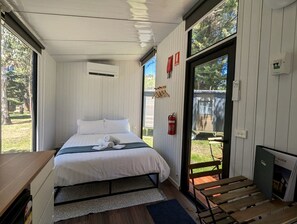 A bedroom with a bed, a small table, a fire extinguisher, and a view of the outdoors. - Fantastic Tiny House Perfect for Families with Swimming Pool, Game Room and Tennis Court in Victoria, Australia (Dadswells Bridge)