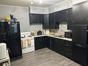 Una cocina con armarios negros, estufa blanca y microondas. En la pared hay un letrero que dice 'thankful'.