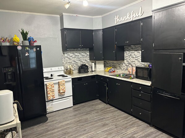 A kitchen with black cabinets, a white stove, and a microwave. There is a sign that says 'thankful' on the wall.
