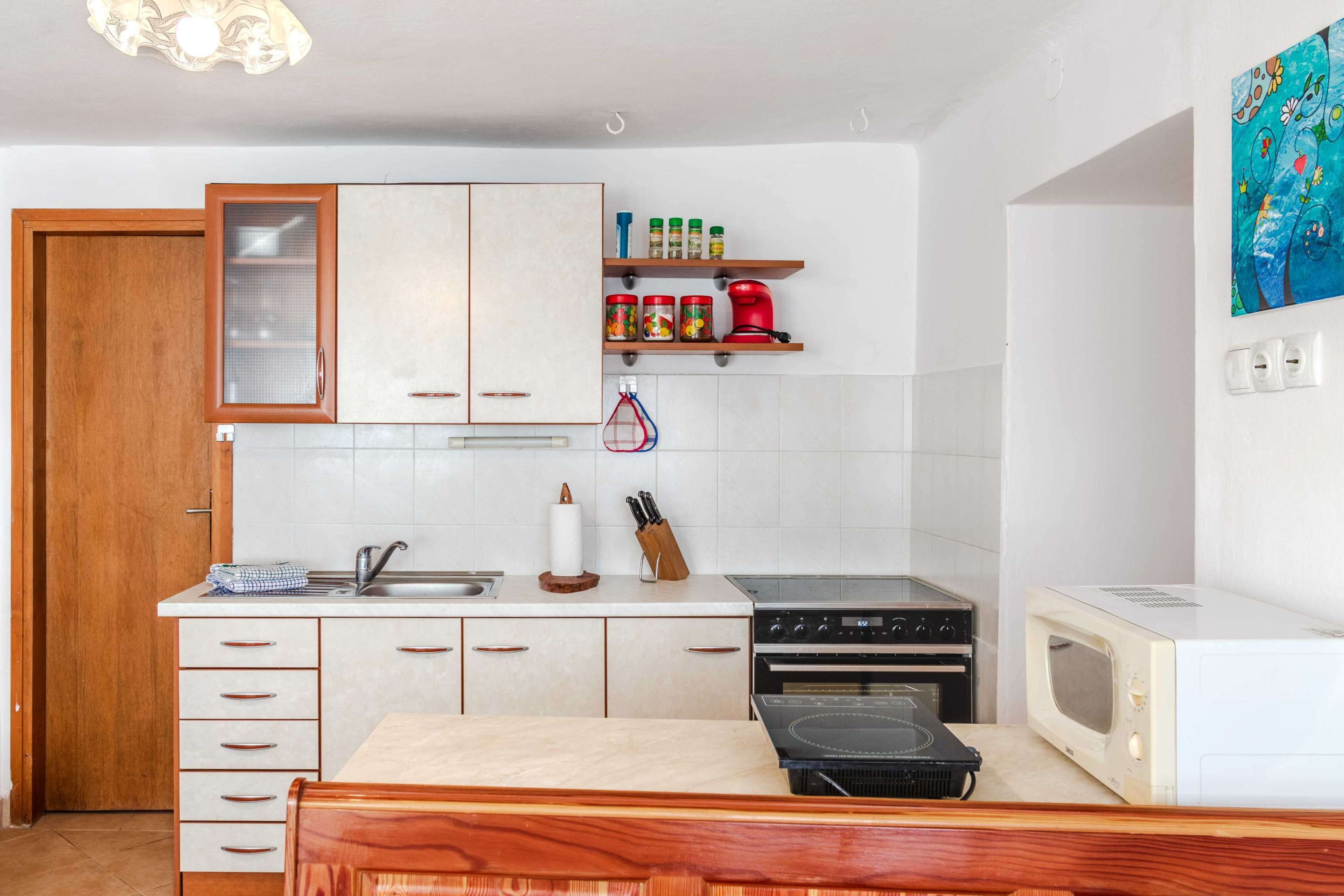 A kitchen with white cabinets, a wooden countertop, a sink, a stove, and a microwave.