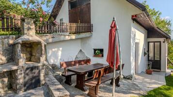A stone-built outdoor seating area with a table and benches, a stone fireplace, and a wooden fence.