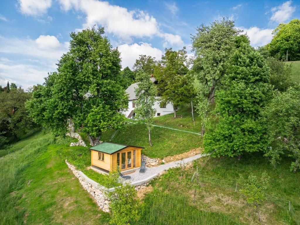 A small wooden cabin with a green roof, surrounded by lush greenery and trees.