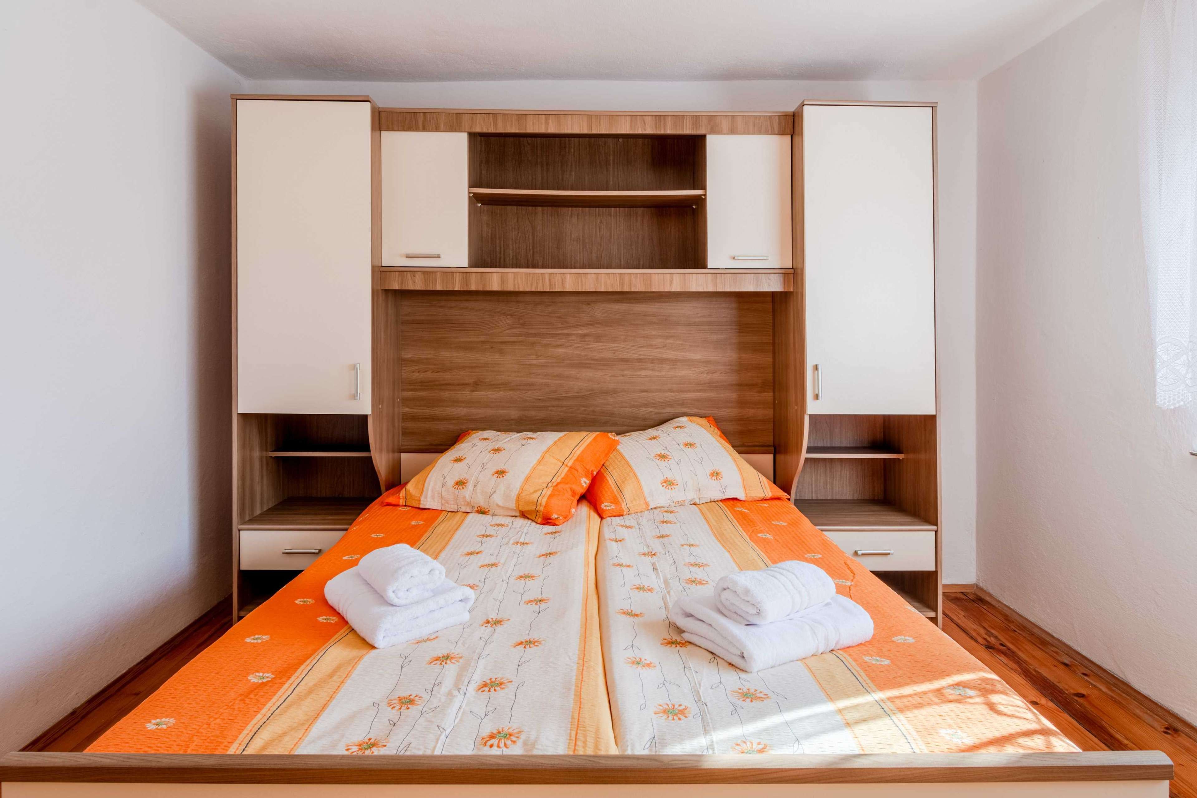 A double bed with a floral bedspread, two nightstands, a wooden headboard, and a wardrobe with open doors.