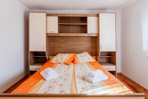 Una cama doble con cubrecama floral, dos mesitas de noche, un cabecero de madera y un armario con las puertas abiertas.