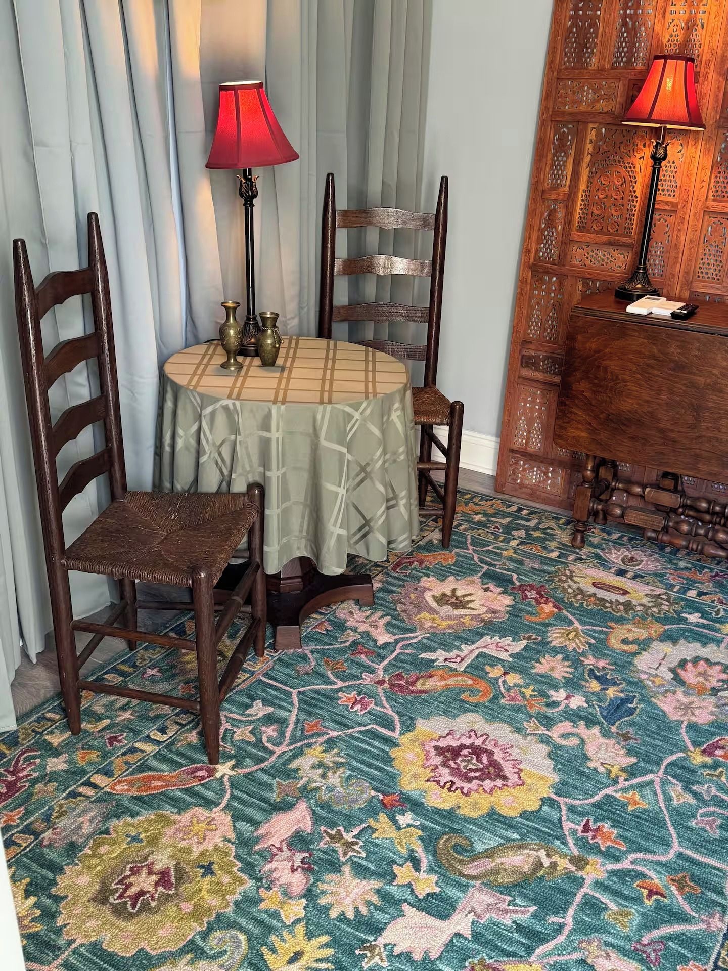 A room with a round table, two chairs, a patterned carpet, and two lamps.