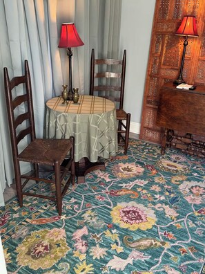 Een kamer met een ronde tafel, twee stoelen, een kamerbreed tapijt en twee lampen.