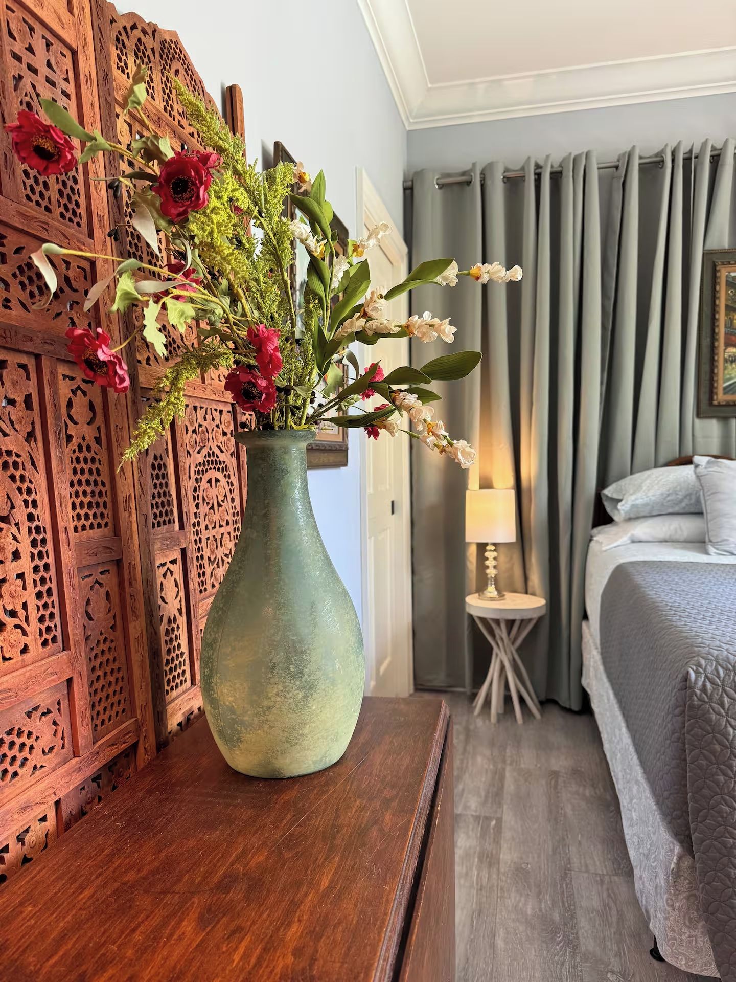Une pièce avec un panneau décoratif en bois, un vase de fleurs, un lit et une lampe.