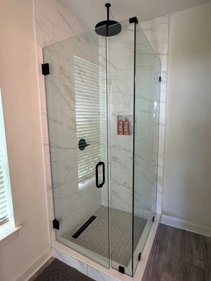 Une douche fermée par des parois en verre, dotée d’une poignée noire et d’une pomme de douche fixée au plafond.