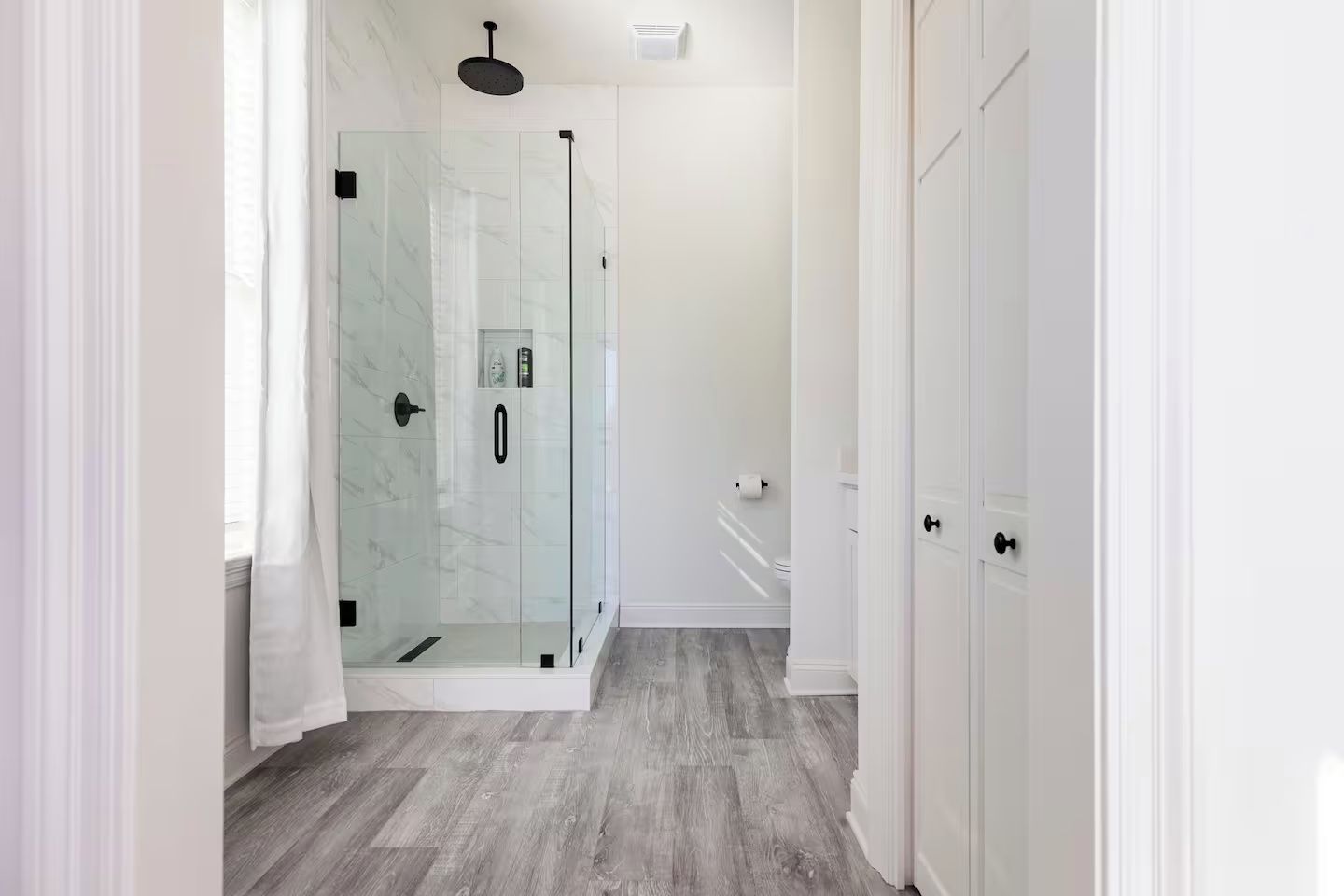 Un baño moderno con cabina de ducha de vidrio, paredes blancas y suelo de madera.