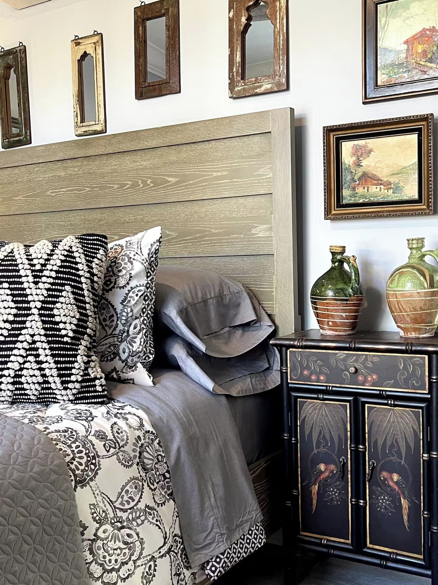 Un dormitorio con cama, almohadas, una mesita de noche con adornos y espejos en la pared.