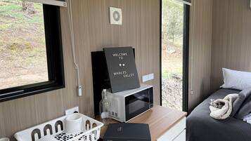 Une chambre moderne avec un lit, un bureau équipé d’un ordinateur, une pancarte sur laquelle on peut lire « BIENVENUE À WHALES VALLEY », et une fenêtre donnant sur l’extérieur.