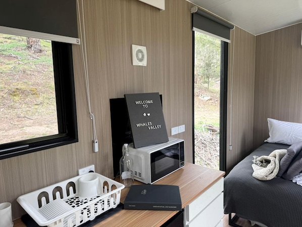 A modern bedroom with a bed, a desk with a computer, a sign reading 'WELCOME TO WHALES VALLEY', and a window with a view of the outdoors.