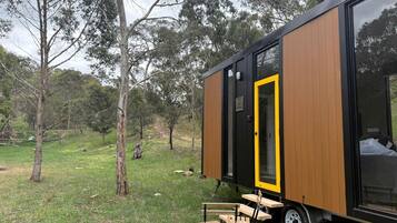 Une maison mobile moderne, de plain-pied, dotée d’une grande porte coulissante, située dans un espace verdoyant avec des arbres en arrière-plan.