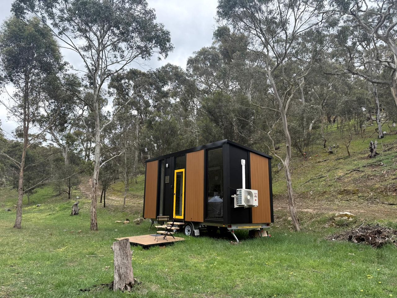 Une petite cabane à un seul étage, dotée d’une porte coulissante, d’un petit porche et d’un climatiseur mobile.