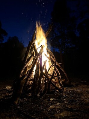 A campfire with visible flames and sparks, surrounded by natural ground and trees. - Off-Grid Tiny House with Cozy Firepit Retreat in Steiglitz, Australia (Steiglitz)